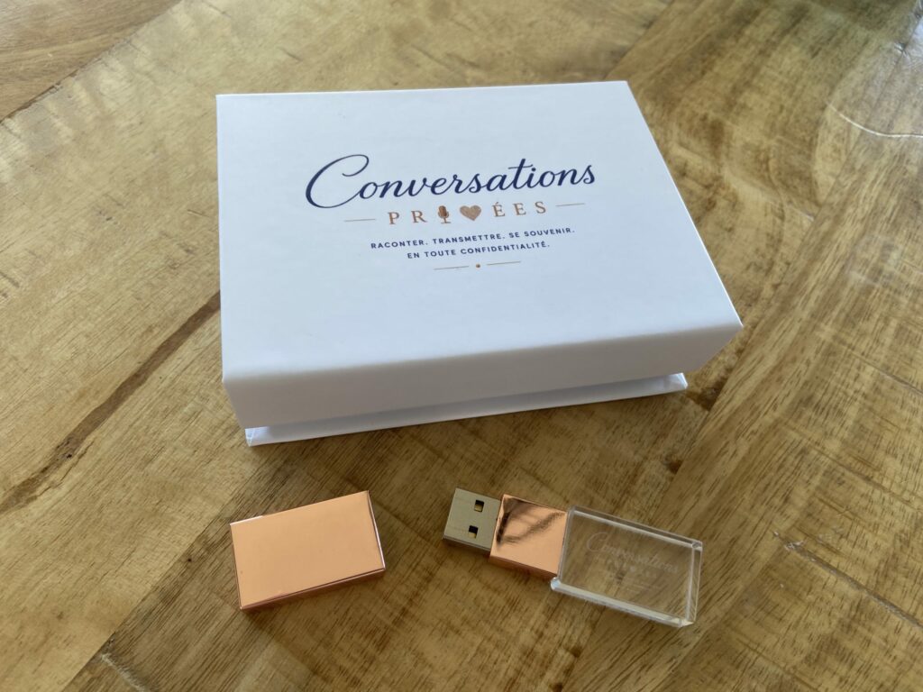 Une petite boîte avec l'inscription Conversations PRIVEES est posée légèrement ouverte sur une table. Une jolie clé USB dorée et transparente est ouverte et posée sur la table devant la boîte. On devine que la clé peut être rangée à l'intérieur de la boîte.